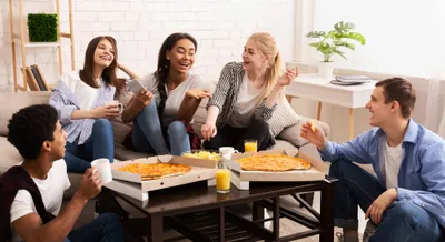 Flatmates sharing pizza and laughing on the sofa in a shared flat