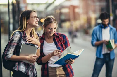 Two students looking at a book together on a city street