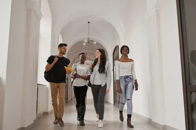 Four students with backpacks walking together down a bright university corridor